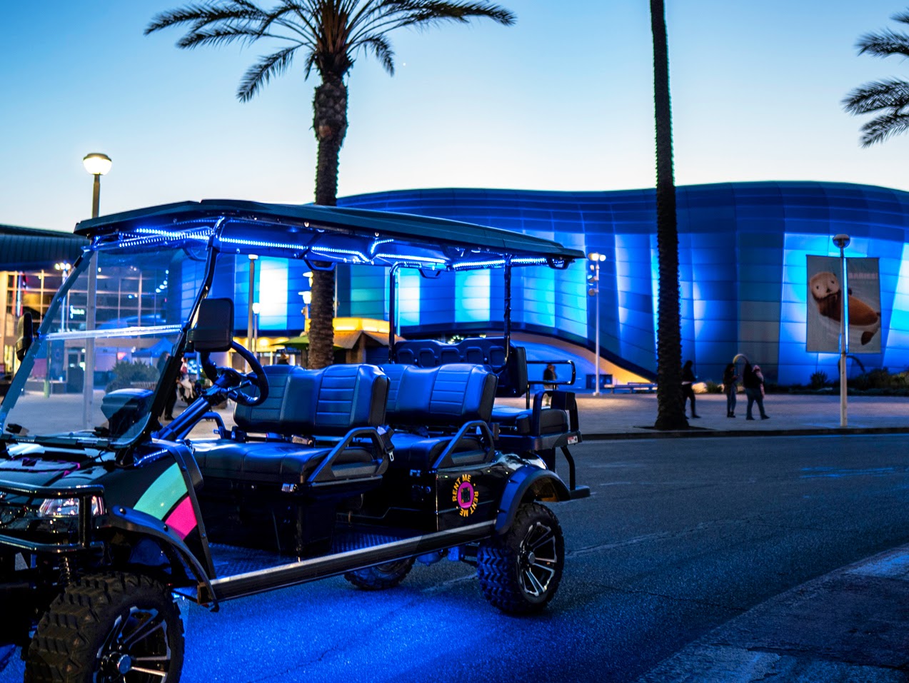 A Driver, Inc. shuttle cart lit with blue LEDs at dusk outside the Aquarium of the Pacific in Long Beach