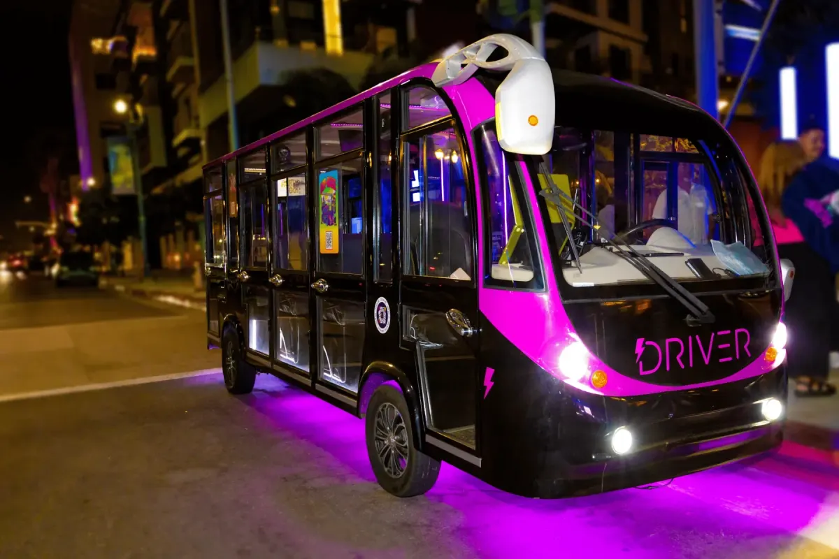 Pink and black Driver tour bus lit with purple lights on a city street at night