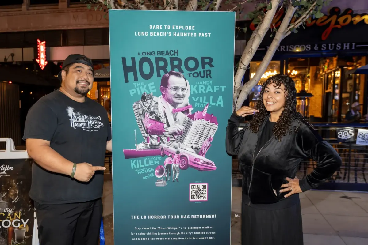 Two guests posing beside the Long Beach Horror Tour poster