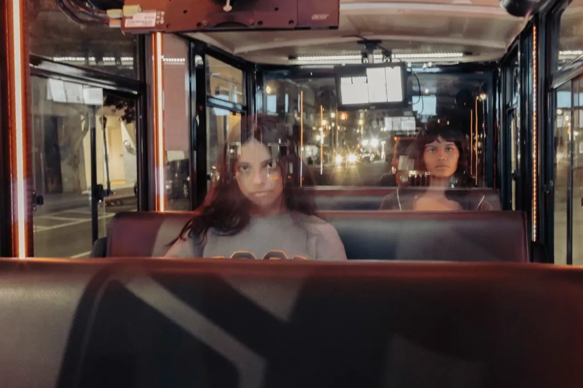 Two guests seated on the tour bus at night, seen through reflections in the glass